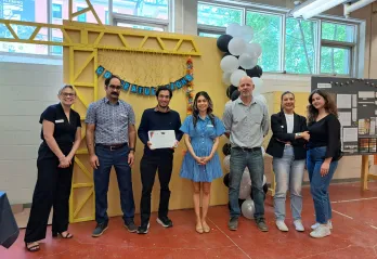 Sushant holding a Power of Trades graduation certificate and standing alongside YMCA staff