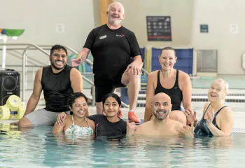 A group of people smiling and posing together in a pool for a photo, showcasing a fun and lively atmosphere.