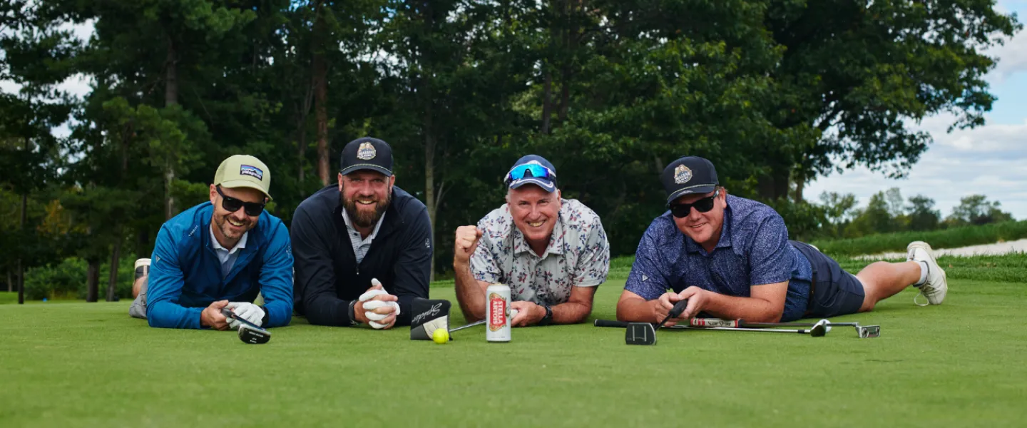 A team of four golfers laying on a golf course and smiling