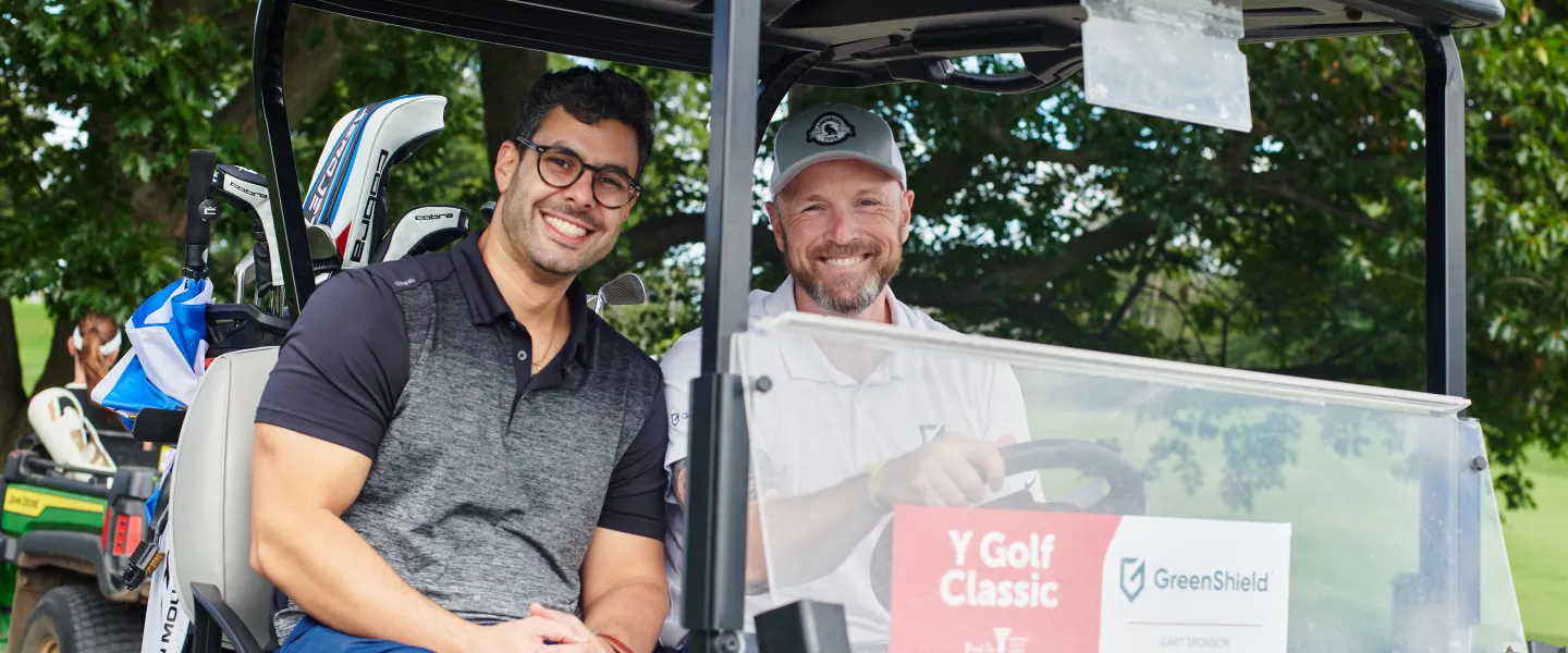 Two men driving a golf cart and smiling.