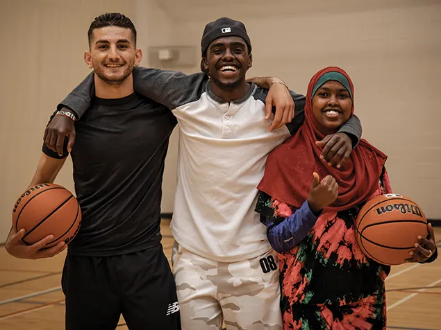 Three young adults playing basketball in the gymnasium.